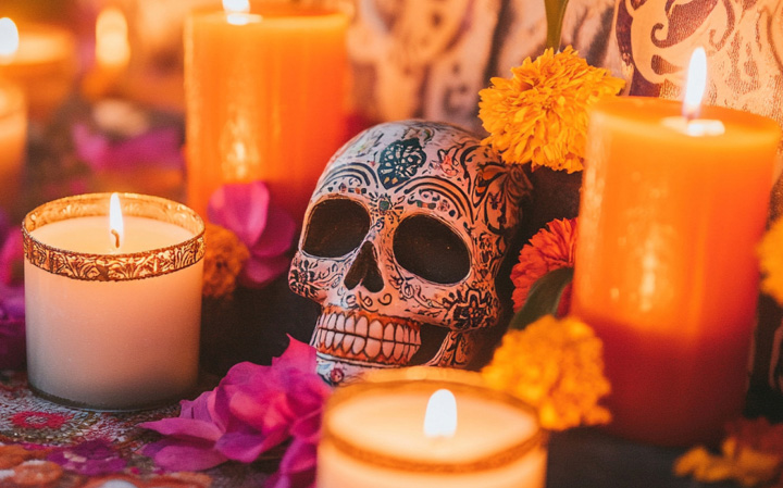 A photo of a sugar candy skull sitting amongst lit candles and flowers on an ofrenda.