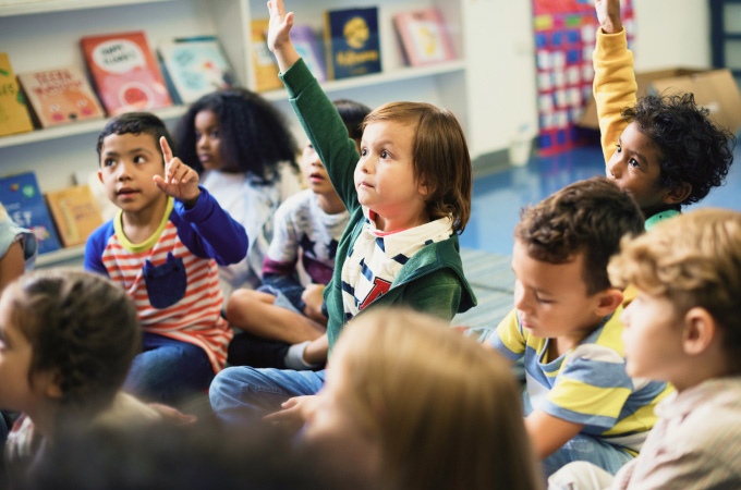 A young student raising their hand in a classroom, enjoying the San Diego Automotive Museum's in-classroom school program
